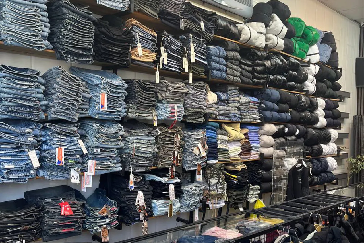 قفسههای فروشگاه بوتیک ایتالیا با چیدمان دقیق از لباسهای تاشده مردانه شامل پلیور، تیشرت و شلوار، با طراحی مدرن و نورپردازی زیبا